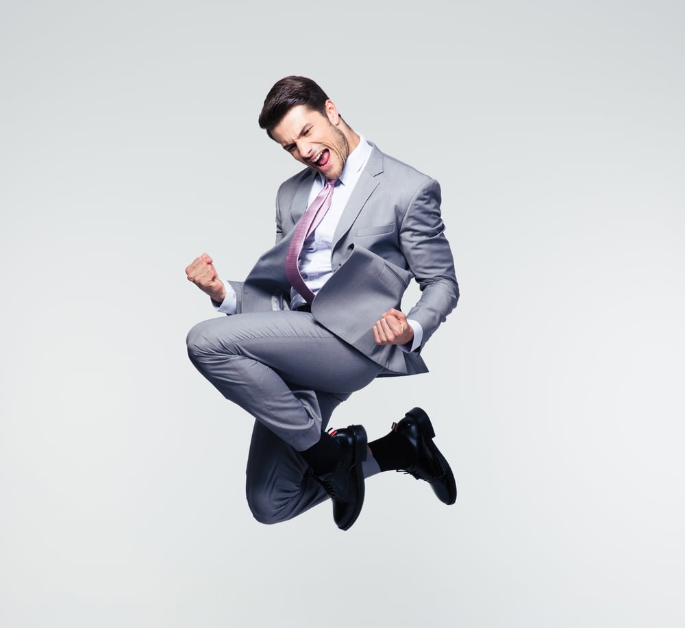 Funny cheerful businessman jumping in air over gray background Funny cheerful businessman jumping in air over gray background